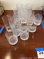 Clear glass drinkware arranged on a wooden surface, mix of short and tall glasses with some cut glass patterns visible.