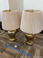 Full view of two brass table lamps with pleated beige fabric shades, showing both lamps and cords.