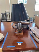 Full view of lamp on table showing black metal shade, cage style lamp body, wooden base with plaque.