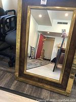 Full view of the rectangular mirror with gold foiled wood frame leaning against wall, showing room reflection