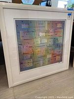 Angled front view of framed lithograph leaning against wall on floor