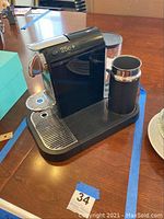 Front-side view of Nespresso 25c+ espresso machine on table showing drip tray and milk frother attachment.