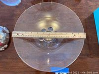 Top-down view of large clear glass bowl with engraved pattern visible on base, approx. 12-inch diameter indicated by wooden ruler.