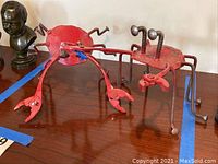 Two red metal crab sculptures constructed from bolts, springs, nuts and clamps on a wooden table with blue tape markings.