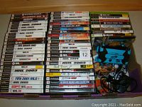 Wide shot of stacked video game cases showing many sports titles mostly for PlayStation 2 including NHL, Madden, FIFA Soccer, NCAA Football, NFL GameDay, Guitar Hero, and others.