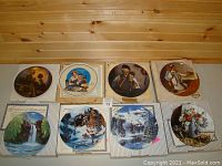 Eight round collector plates laid out on wooden floor, showing renewal of various artwork themes, including wildlife and domestic scenes.