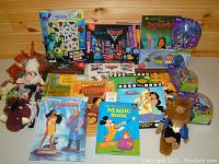 Disney books and toys laid out on wooden surface including books of Pocahontas, Aladdin, Bambi, Pinocchio, Lady and the Tramp popup book, and Mickey Mouse Magic book. Also visible are two bubble magnet books featuring Monsters Inc, a boxed Disney Cars Tow Mater toy vehicle, and other Disney character toys.