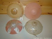 Four vintage ceiling light shades displayed on flat surface showing variation in color and decorative patterns