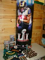 Large NFL Super Bowl LI poster with football player in uniform, surrounded by various football trading cards, small figurines, and jerseys including 'Levens' jersey.