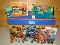 Wide shot showing the toy trunk, carrying case, multiple Skylanders figures lined up, and two Skylanders Universe comic books.