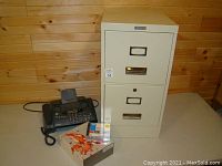 Beige two-drawer metal file cabinet next to HP fax machine, SoftImage software and DVD+R discs visible in front