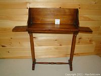 Full front view of the small mid century wooden table with pull out sides extended and a backrest attached at the rear.