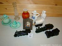 Multiple collectibles including Avon bottles, white ceramic pieces, red vase, black train set, glass candle holder, and framed miniature portrait.