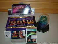 Lot showing unopened Star Trek Voyager Season One trading card packs in original box, Star Trek The Next Generation trading cards, and a greenish-blue mini statue under dome.