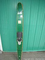 Full length view of a single wooden water ski with green stain and black foot binding mounted centrally.