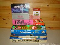 Photo showing stacked board games including Mindtrap, Trivial Pursuit, The Badass Girls Poker Party, Yahtzee, Scene It?, Advance to Boardwalk, Friends, Ultraviolet, and Billionaire.