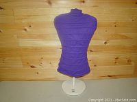 Front view of the purple fabric-covered small dress form bust on a wooden wall background.