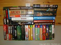 Full lot view showing multiple fantasy and young adult books stacked on a wood surface. Titles include Narnia, Hunger Games, Game of Thrones, Dune, and others.
