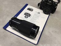 Nikon EM 35mm camera with zoom lens and instruction manual shown beside it on floor.