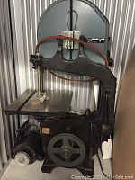 Delta 14” bandsaw showing cast iron base, tabletop, head and motor assembly with red drive belt looped around wheels