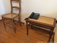 One caned hardwood chair with turned legs beside a small hardwood table with rectangular caned top, featuring a phone on it.
