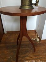 Round-top cherrywood three-legged table with solid wood surface and gently curved legs seen from side.