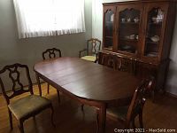 Dining table and chairs arranged in dining room, showing shape, wood finish, and upholstery