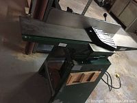 Front side view of green painted metal jointer on integrated stand