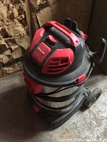 Photo showing red and black Shop-Vac with stainless steel canister and hose attached around base