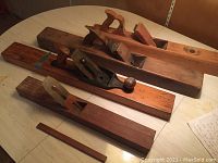 Wide angle photo of five hand planes on a light table showing variety in size and style, including wooden and metal-bodied planes.
