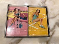 Two decks of Duratone playing cards in original boxes, one pink themed with a bowling girl and one yellow themed with a tennis girl