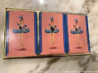Set of three playing card decks in pink boxes with ballerina illustration under gold-toned outer box lid.