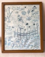 Full front view of the framed embroidery needlework art showing bird, flowers, text, and fence design in blue thread on white fabric within a wooden frame.