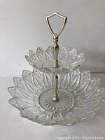 Clear iridescent glass two-tier serving dish shown against a plain background to highlight the glass design and metal handle.