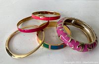 Five bangle bracelets in gold-tone and enamel, displayed grouped with some overlapping. Colors include gold, pink, turquoise.