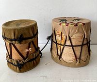 Two vintage First Nations style mini drums, one brown leather with black lacing and feather, one birch bark with painted leather top and black lacing.