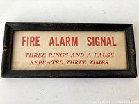 Rectangular black wooden framed fire alarm sign with red text instructions on white background.