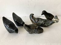 Five carved soapstone figures arranged on a white surface, showing overall lot content and detail of each piece.