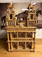 Front view of large rattan bird cage shaped with four sides, two resembling tall towers and a center opening decorated with round detail.