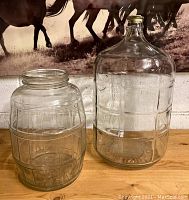 Two large clear glass jars side by side on a wooden surface with a horse picture in the background.