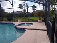 Wide view of two white resin planters with plants positioned on pool deck by screen enclosure with outdoor scenery.