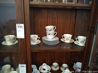 Display of tea cups and saucers of two brands in glass cabinet