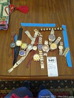 Photo of 13 assorted watches laid flat on a wooden floor showcasing various straps, dials, and styles.