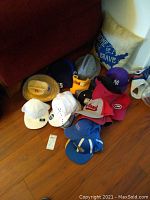 Overview of hats grouped on floor including various baseball caps, wool hats, and a pillow with patriotic theme.