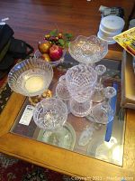 Photo showing various crystal and cut glass vases, bowls, and decanter arranged on a glass table.