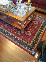 Full view of the red and blue Saint Honore area rug underneath a wooden coffee table, showing the overall size and pattern