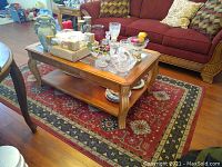 Full view of wood coffee table with decorative items on top and shelf below on red patterned rug