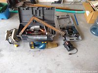 Overview photo showing toolbox open with various hand tools inside including a square ruler, plus electric circular saw, cordless drill case, vacuum, and staplers arranged in front