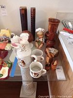 Ceramic owl-themed teapot, cups, figurine girl with chef hat, wooden vases and incense holders on glass shelf.