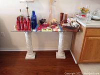 Full view of glass top table with columns, showing several items on the table and the floor and kitchen nearby.